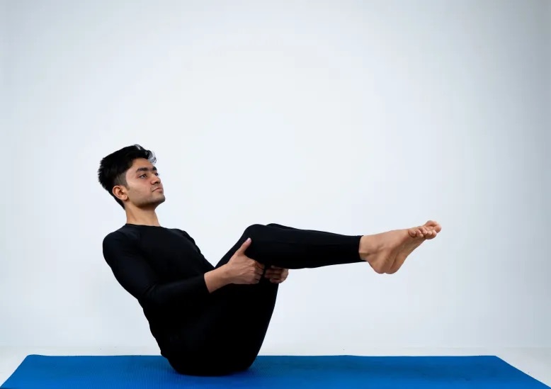 A man practicing the half-boat pose (ardha navasana) of yoga