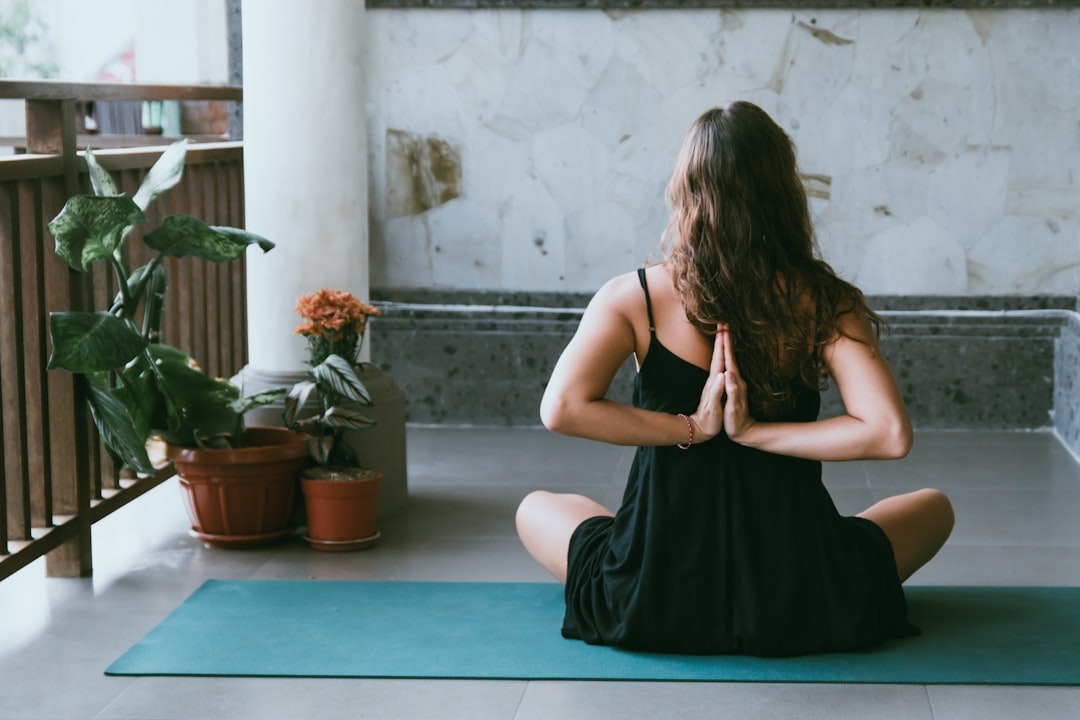 A woman seen from behind practicing a somatic yoga movement by joining both hands on her back.