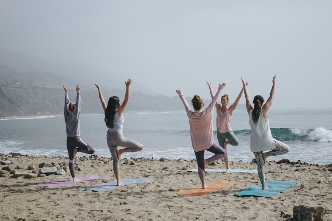 A group of five women on a beach practicing somatic yoga movements.