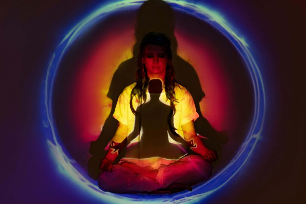 Woman in a yellow jacket and blue denim jeans sitting with blue round ring around her, meditating and uttering chakra affirmations.